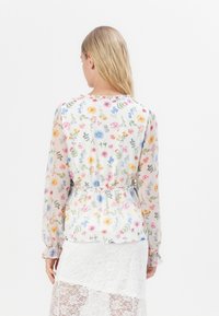 Blusa floreale a maniche lunghe, tessuto leggero e trasparente, stampa floreale multicolore su sfondo chiaro, vita elastica con maniche arricciate.