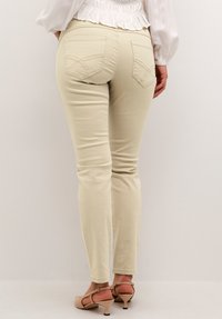Beige skinny jeans med skrå baglommer, glat tekstur og tætsiddende design, kombineret med lyse beige højhælede sko.