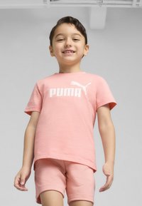 Rožinė medvilninė marškinėliai trumpomis rankovėmis su balta "PUMA" logotipo, derinami su atitinkančiomis rožinėmis šortais. Sukurtas vaikams. Lygi tekstūra.