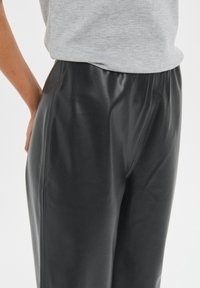 Pantalones de cuero negro con una textura suave y pretina elástica, que presentan un corte relajado y detalles de costura sutiles.
