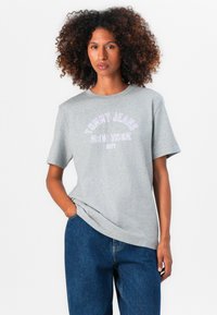 T-shirt en coton gris avec col ras du cou. Présente un texte violet indiquant "TOMMY JEANS NEW YORK CITY" dans un design courbé. Manches courtes, coupe décontractée.