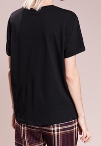 Czarny t-shirt z krótkim rękawem, wykonany z bawełny, z okrągłym dekoltem, w luźnym kroju, pokazany od tyłu z gładkim wzorem. W zestawie z spodniami w kratę.