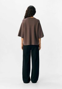 Débardeur tricoté marron avec des manches larges associé à un pantalon noir loose. Texture lisse, coupe décontractée et design minimaliste.
