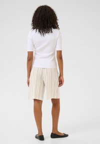 Haut à manches courtes blanc côtelé associé à un short rayé beige clair, présentant une coupe décontractée et atteignant le milieu de la cuisse. Chaussures plates noires.