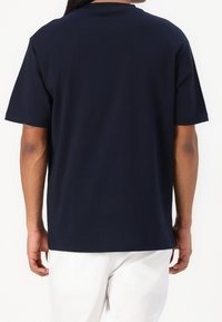 Granatowa bawełniana koszulka z luźnym krojem, krótkimi rękawami i okrągłym dekoltem, przedstawiona z tyłu, z minimalnymi detalami szycia.