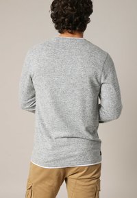 Grauer langärmliger Pullover aus strukturiertem Stoff, runder Ausschnitt und gerippte Bündchen. Dezente Kontrastnähte am Saum und an den Schultern.