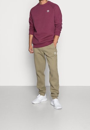 Bordeauxfarbener Sweatshirt mit gerippten Bündchen und Rundhalsausschnitt, kombiniert mit olivgrünen Jogginghosen mit Seitentaschen, weißem Logo und weißen Sneakers.