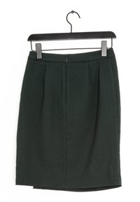 Tmavě zelená tužková sukně s hladkým povrchem, s čistým zipem na zadní straně a dvěma předními sklady. Visí na černém plastovém ramínku.