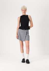 Čierny top bez rukávov s gombíkovým detailom, doplnený mini sukňou s houndstooth vzorom. Nosené s bielymi ponožkami a čiernymi topánkami.