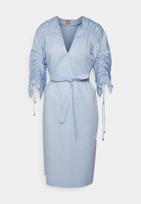 Robe bleu clair en tissu lisse avec un décolleté en V profond, manches bouffantes froncées, taille cintrée avec une ceinture et cordons décoratifs.