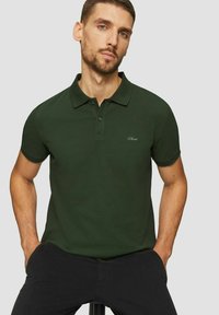 Dunkelgrünes Polohemd aus strukturiertem Stoff, mit klassischem Kragen, drei Knöpfen und einem bestickten Logo auf der Brust.
