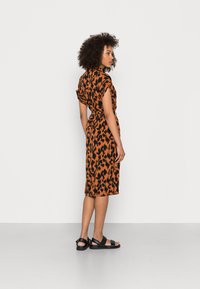 Rochie cu imprimeu leopard portocalie și neagră, cu mâneci scurte, talie accentuată și lungime până la genunchi. Modelul poartă sandale negre, stând pe un fundal neutru.