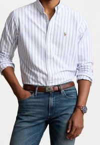 Gestreept button-down shirt in wit en lichtblauw, van katoen, met een klassieke kraag. Bruine leren riem en blauwe denim jeans.