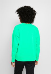 Sudadera verde de cuello redondo, hecha de tejido suave, con mangas largas y puños acanalados. Presenta un corte relajado con un dobladillo recto.