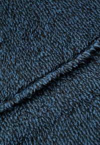 Weicher, plüschiger Stoff in unterschiedlichen Schattierungen von Dunkelblau mit einer strukturierten Oberfläche und einem gedrehten Fransenrand, der Tiefe und Dimension schafft.