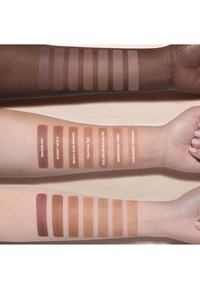 Campioni di bronzer su tre tonalità di pelle: scura, media e chiara. Le tonalità includono marroni profondi e abbronzature calde, etichettate con nomi. Texture liscia.