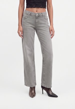Femme portant un jean gris taille haute coupe droite, un crop top en dentelle noir et des bottines noires à talons hauts à bout pointu.