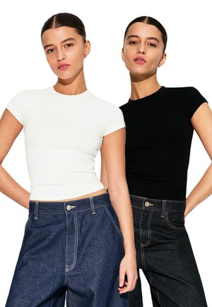 Two fitted short-sleeve t-shirts in white and black, paired with high-waisted denim pants. Smooth texture, round necklines, no visible patterns.