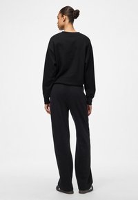 Zwarte trui en bijpassende broek. Zachte, comfortabele stof. Losse pasvorm met lange mouwen en wijde pijpen. Eenvoudig, minimalistisch ontwerp zonder patronen.