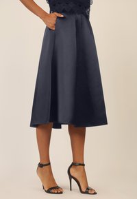 Gonna A-line blu navy realizzata in tessuto morbido, con tasche laterali e un taglio alla lunghezza del ginocchio; abbinata a sandali neri con tacco alto e cinturini.