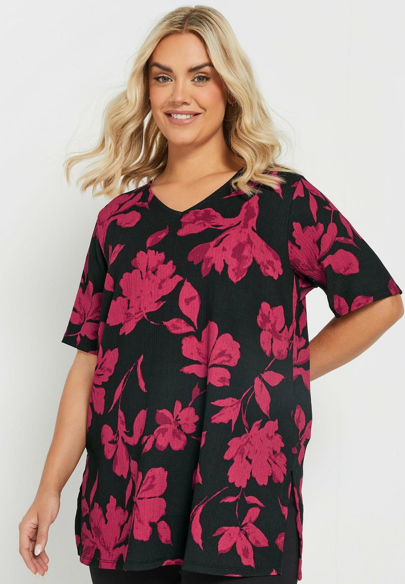 Top negro de flores con mangas cortas, que presenta patrones de flores rosas y un diseño de escote en V. La tela parece tener textura y cuenta con aberturas laterales.