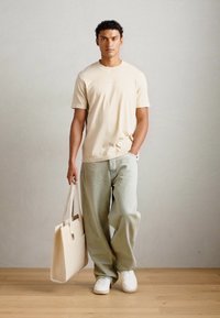 Beige cotton t-shirt paired with light green baggy jeans. White sneakers and a cream-colored tote bag with a rectangular shape.