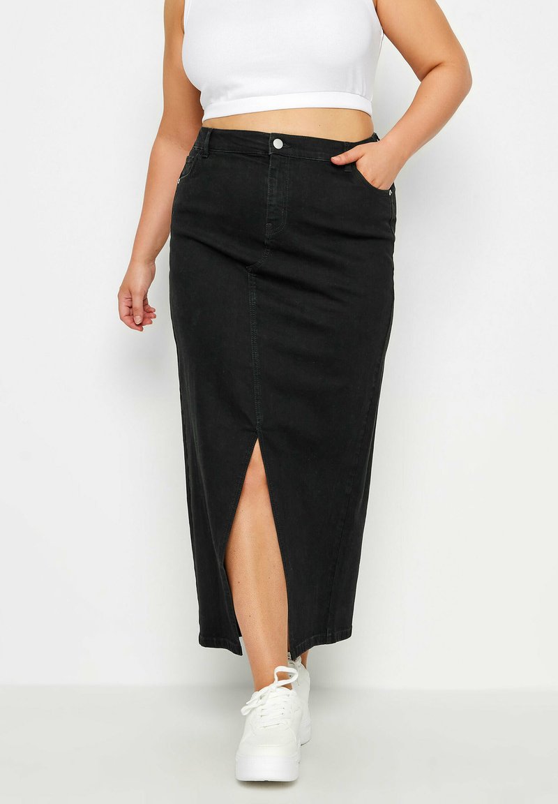 Jupe maxi en denim noir avec une fente à l'avant, deux poches et une coupe ajustée. Assortie à des baskets blanches et un top court.