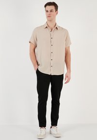 Korte mouwen beige shirt met marineblauwe knopen, gecombineerd met slim zwarte broek en witte sneakers met tan en grijze accenten.