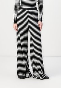 Pantalons larges à rayures noires et blanches, avec une texture lisse, un tissu extensible et une taille noire. Convient pour un usage décontracté.