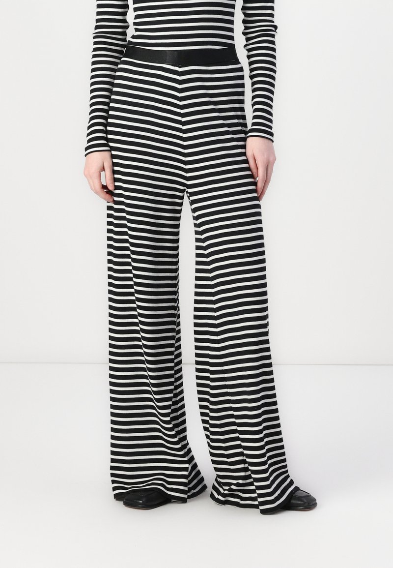 Pantalons larges à rayures noires et blanches, avec une texture lisse, un tissu extensible et une taille noire. Convient pour un usage décontracté.