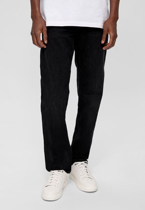 Schwarze Denim-Hosen mit geradem Bein und glatter Textur, getragen mit weißen Sneakers mit runder Zehenpartie und flacher Sohle.
