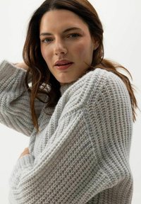 Világosszürke kötött pulóver texturált mintával, lazább szabással és oversized ujjal, a kényelem és melegség érdekében tervezve.