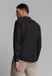 Zwarte blouse met lange mouwen in een lichtgewicht stof, met een rechte snit en knoopmanchetten. Bevat een klassieke kraag en een subtiele textuur.
