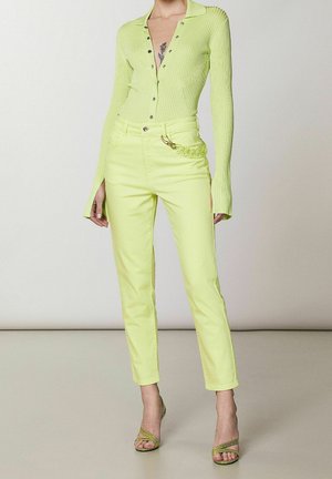 Neonvihreä ribbineulottu pitkähiha-paita, jossa napit, ja korkeavyötäröiset kapenevat housut; varustettu kiiltävillä metalliosilla ja ketjusomisteella taskussa.