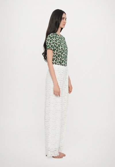 Top aderente con fantasia floreale verde abbinato a pantaloni larghi bianchi in pizzo. Tessuto morbido, maniche corte e scollo rotondo.