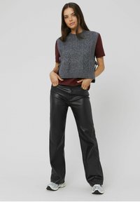 Gilet en tricot gris avec un motif en torsade sur une chemise bordeaux, associé à un pantalon en cuir noir et des baskets grises. Fond neutre.