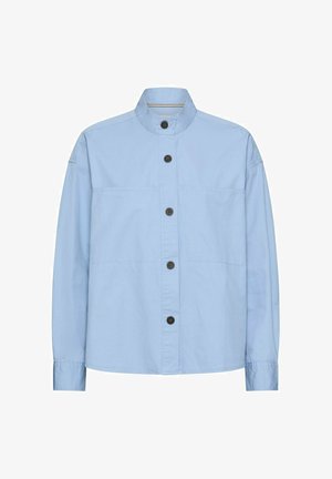 Jasnoniebieska koszula z długim rękawem i stójką, z pięcioma czarnymi guzikami na przodzie oraz widocznym poziomym przeszyciem na wysokości klatki piersiowej i rękawów.