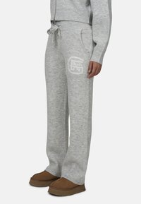 Szare dzianinowe spodnie dresowe z wiązaniem w pasie, bocznymi kieszeniami oraz subtelnym detalem z logo. Teksturowany materiał i ściągacze przy nogawkach dla komfortu.