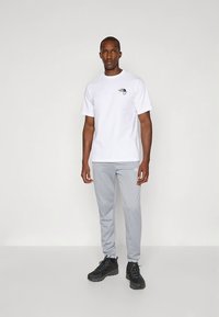Biele tričko s krátkymi rukávmi a logom, skombinované so svetlosivými teplákmi a čiernymi športovými topánkami. Hladká látka, ležérny strih.