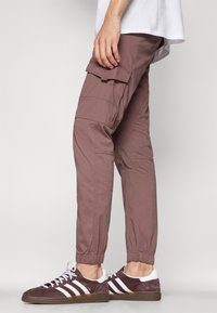 Cargobroek in stofroze, met elastische boorden, zijzakken, gladde stof, gecombineerd met donker bordeaux sneakers met witte strepen.