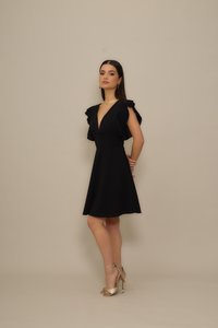 Black A-line dress with ruffled sleeves, deep V-neckline, and smooth fabric. Complemented by gold heeled sandals.