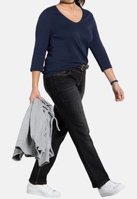 Námořnický v-neck dlouhý rukáv top v kombinaci s černými džíny a bílými teniskami. Osoba drží šedou mikinu.