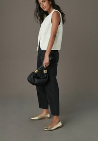 Veste sans manches matelassée blanche, jean noir taille haute, ballerines dorées avec un détail en nœud, et un sac noir froncé avec des accents dorés.