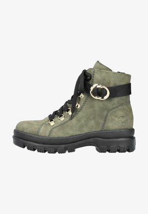 Bottes de cheville en daim vert avec semelle en caoutchouc noire. Les caractéristiques incluent des œillets en métal, des lacets noirs et un détail de boucle circulaire décorative.