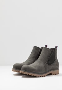 Pár šedých kožených kotníkových bot s elastickými bočními panely, hnědými gumovými podrážkami a poutky s červenými a modrými pruhy.