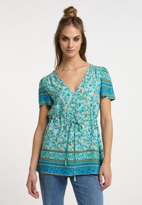 Türkise Blumen-Tunika mit kurzen Ärmeln, V-Ausschnitt, Kordelzug in der Taille und gemusterten blauen Akzenten. Leichter Stoff mit weicher Textur.