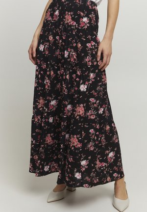 Czarna długa spódnica maxi w różowo-biały kwiatowy wzór, z marszczonym stanem, noszona z białymi butami na obcasie z ostrym czubkiem.