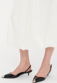 Svarta lackläders slingbacksandaler med spetsig tå och silvermetalliska detaljer, med en låg kittenklack och en elegant design.