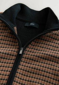 Pulover cu fermoar, cu guler negru; are un material cu motive în nuanțe de brown și negru. Fermoar argintiu și eticheta "NEXT" vizibilă. Textură moale.