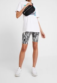 Černobílé zebrované cyklistické šortky, spárované s bílým grafickým tričkem a bílými teniskami. Také je přítomná malá černá kabelka přes rameno.